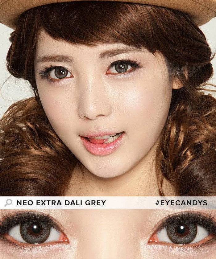 A young woman with curly brown hair wears a brown hat and NEO Vision Extra Dali Grey color contact lenses by NEO Vision, smiling playfully. A close-up highlights the grey lenses in her eyes with text: "NEO EXTRA DALI GREY #EYECANDYS.
