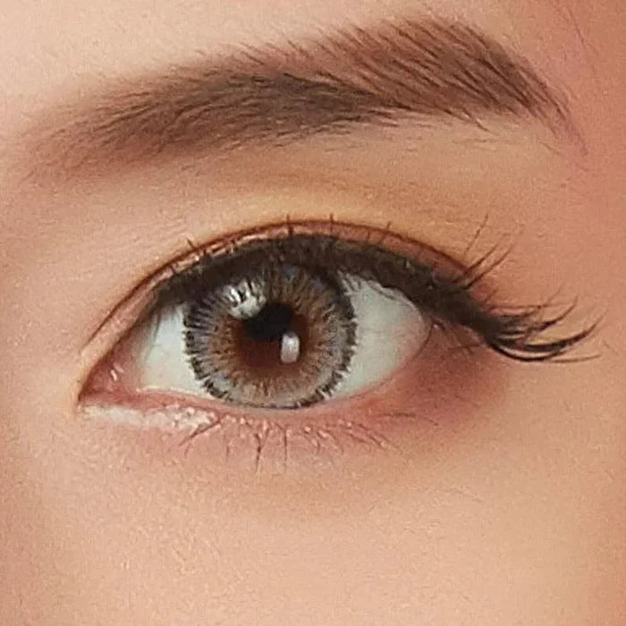 A close-up of a brown eye with long lashes and a defined brow, enhanced by NEO Vision Glamour Grey (Custom Toric for Astigmatism) contacts, highlighting natural makeup and subtle elegance.