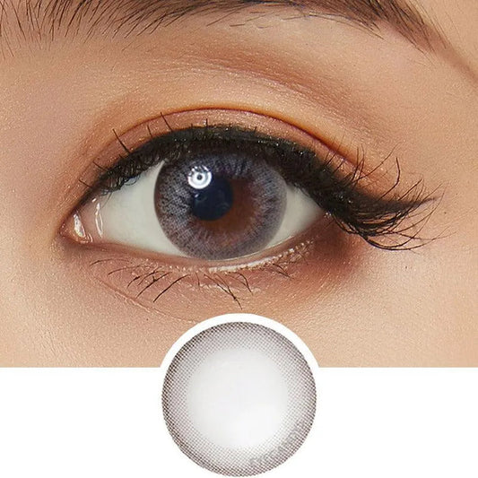 A close-up of an eye wearing NEO Vision Monet Grey (Custom Toric for Astigmatism) lenses by NEO Vision, cosmetic contacts that enlarge the iris with a soft grey hue. Below is a close-up of the lens showing its subtle gray ring design.