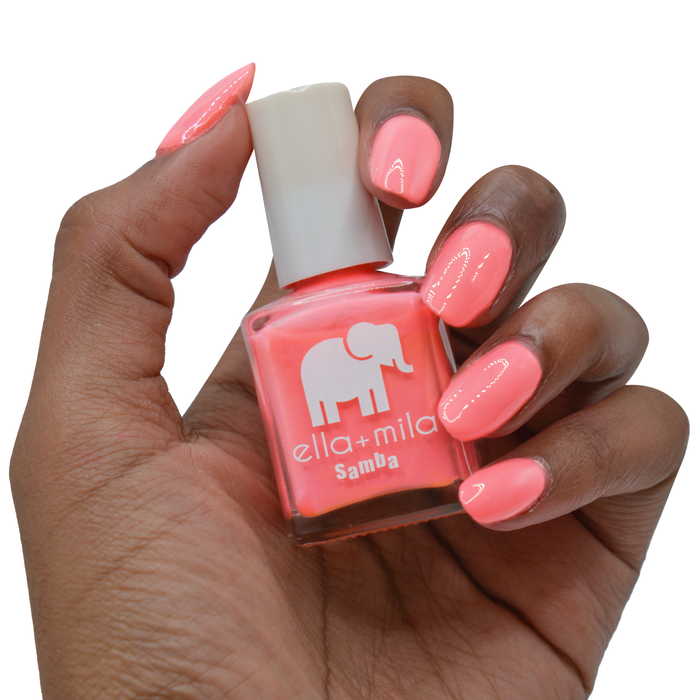 Pinktini coral pink nail polish on a deep skin tone, hand holding the bottle