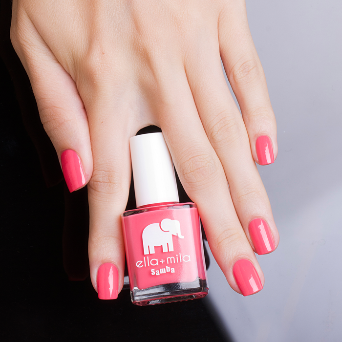 Pinktini coral pink nail polish manicure on a light skin tone, hand resting beside the bottle
