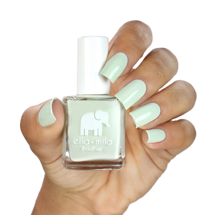 Pistache pastel green nail polish on a medium-deep skin tone, hand holding the bottle