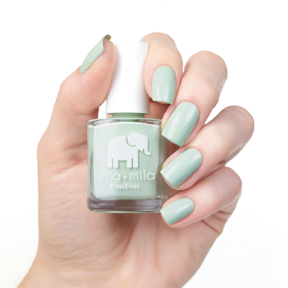 Pistache pale green nail polish manicure on a light skin tone, holding the bottle