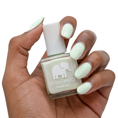 Pistache pastel green nail polish on a deep skin tone, hand holding the bottle