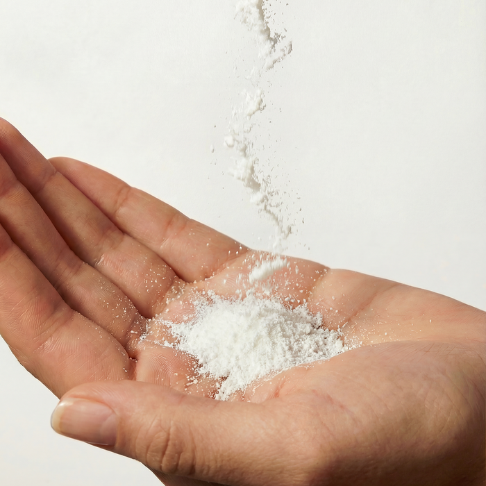 A close-up of a person's open palm holding a small pile of white powder, with more white powder falling into the hand against a plain light background.