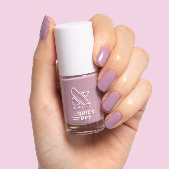 Hand holding bottle of Prairie nail polish with nails painted in soft blooming purple polish by Olive and June