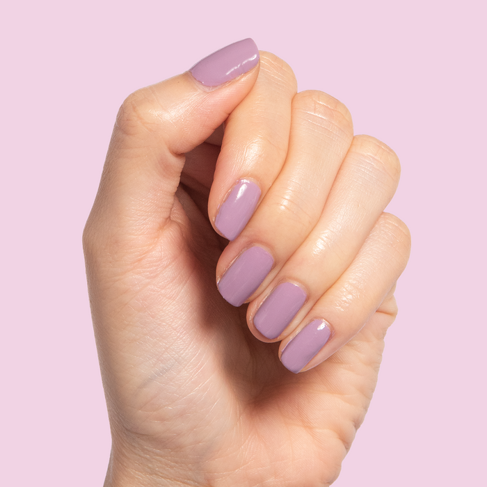 Hand with nails painted in glossy Prairie polish showing a smooth, blooming purple manicure by Olive and June