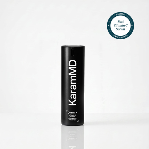 A black cylindrical KaramMD Quench Vitamin C serum bottle standing upright on a white reflective surface, with a teal circular award badge in the top right corner.