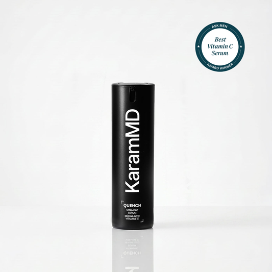 A black cylindrical KaramMD Quench Vitamin C serum bottle standing upright on a white reflective surface, with a teal circular award badge in the top right corner.