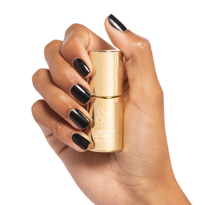 Hand holding Olive and June Quick Dry Top Coat bottle with glossy black polished nails in bright light