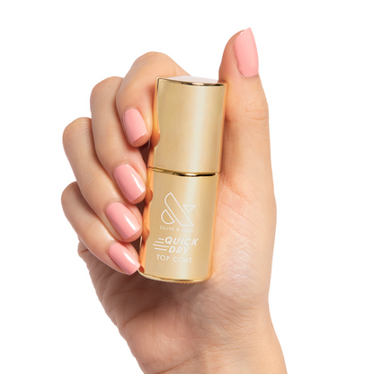 Hand with pink manicured nails holding Olive and June Quick Dry Top Coat bottle for shiny at home manicure
