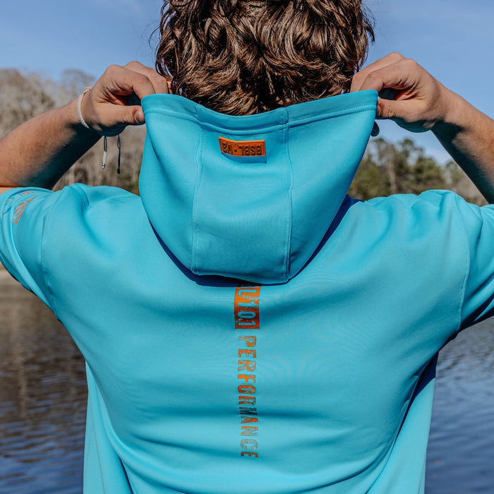 Person wearing a blue short sleeve hoodie with branding, standing by a body of water.