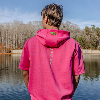 Person wearing a pink hoodie with BSBL SZN logo, standing by a lake with trees in the background.