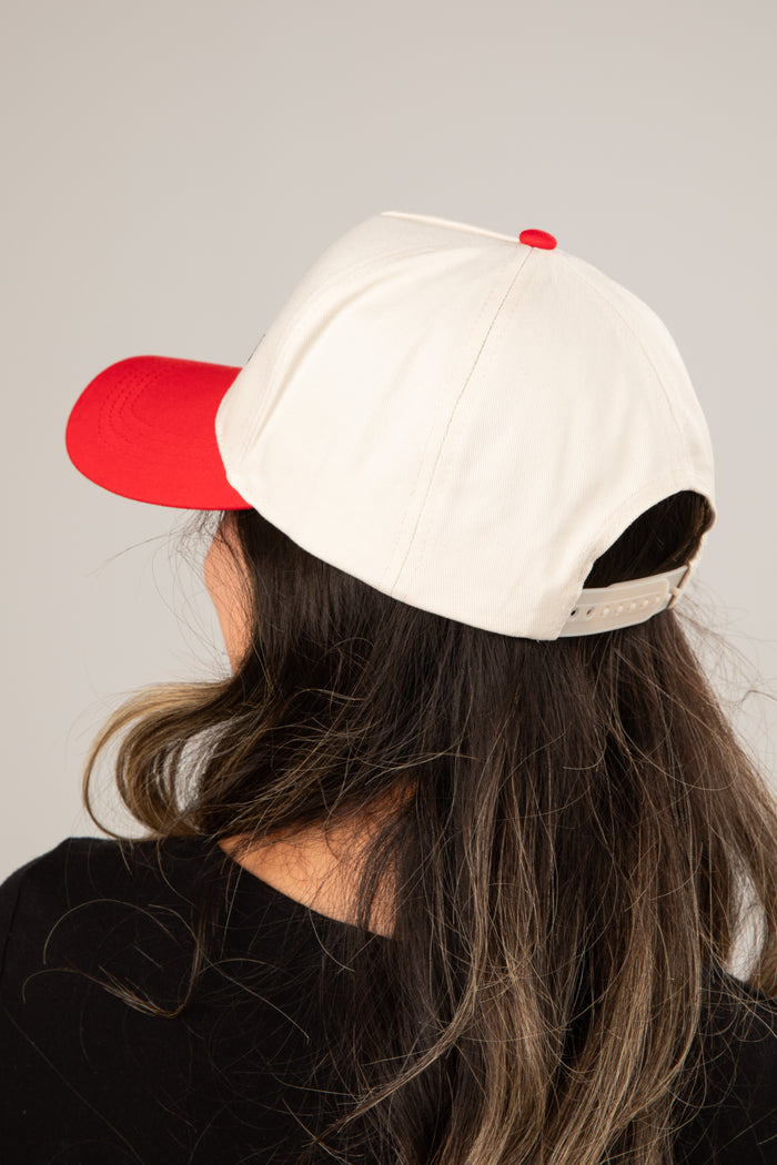 Person wearing a white cap with a red bill on a plain background