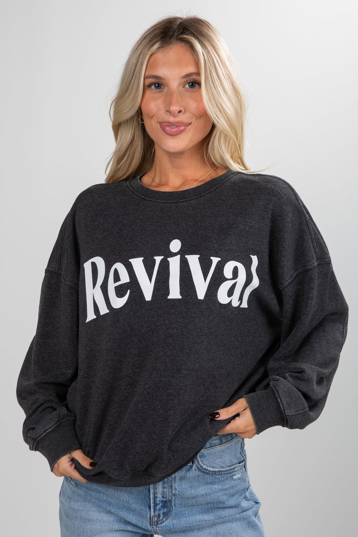 Woman wearing a black sweatshirt with 'Revival' text on a plain background