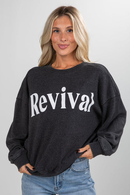 Woman wearing a black sweatshirt with 'Revival' text on a plain background