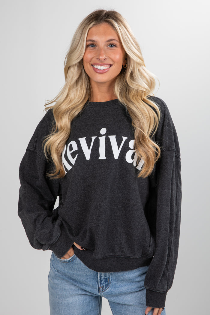 Woman wearing a black sweatshirt with 'revival' text on a plain background