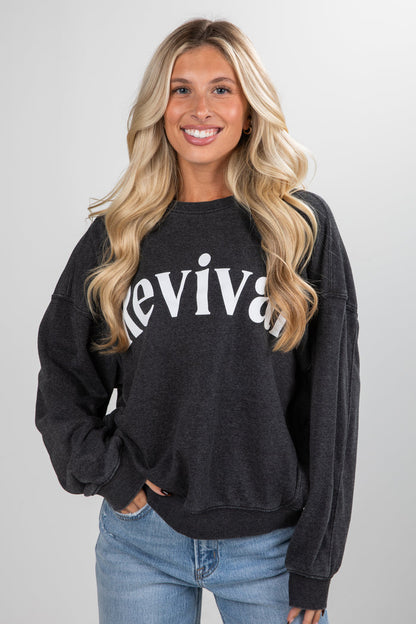 Woman wearing a black sweatshirt with 'revival' text on a plain background