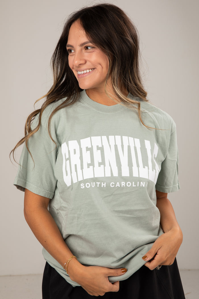 Woman wearing a green t-shirt with 'Greenville South Carolina' text on a plain background