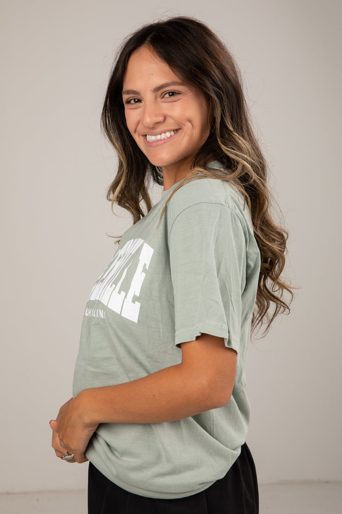 Woman wearing a light green t-shirt with text, standing against a plain background