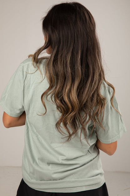 Person wearing a light green shirt with long, wavy hair on a plain background