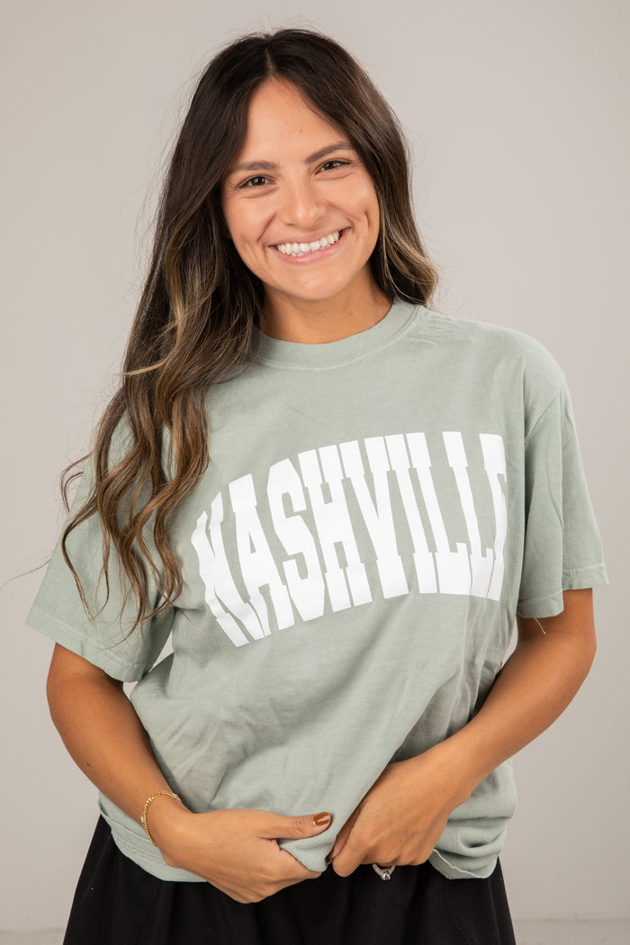 Woman wearing a green t-shirt with 'Nashville' printed on it against a plain background