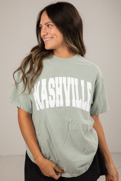 Woman wearing a green t-shirt with 'Nashville' printed on it against a plain background