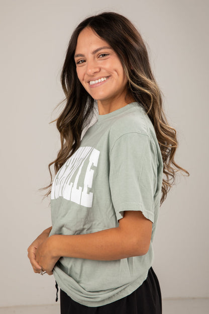 Woman wearing a green t-shirt with text, standing against a plain background