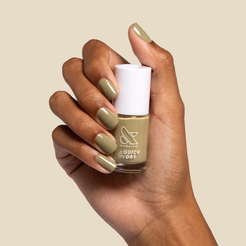 Hand with nails painted in Olive and June Sagey green polish holding quick dry nail polish bottle against beige background