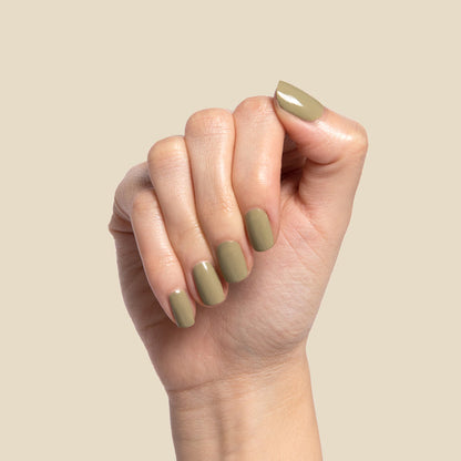 Hand with nails painted in glossy Sagey polish with muted green shade against a neutral background for manicure display