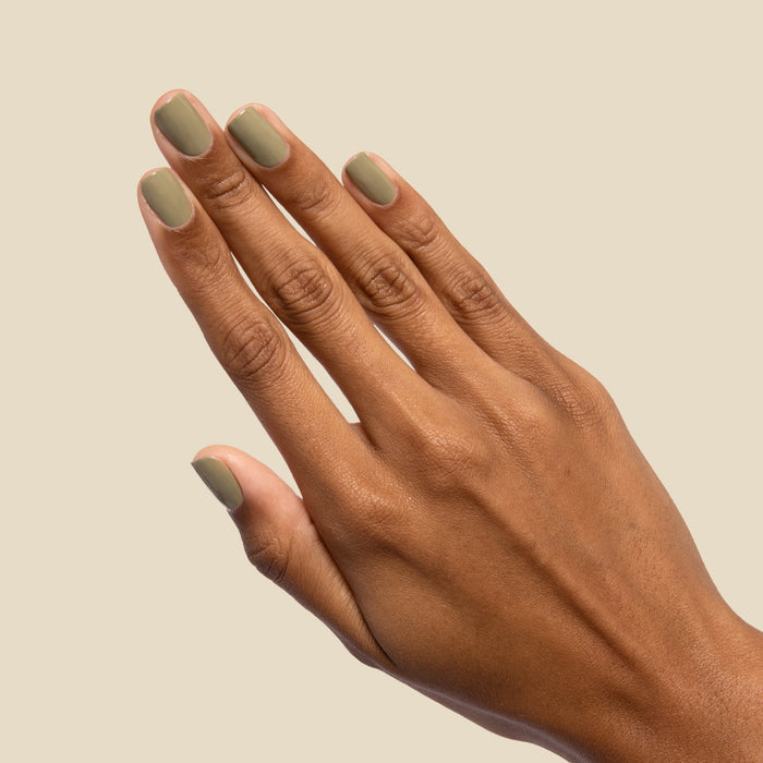 Hand with nails painted in mid-tone Sagey polish by Olive and June against a soft beige background for manicure display