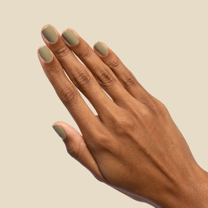 Hand with nails painted in mid-tone Sagey polish by Olive and June against a soft beige background for manicure display