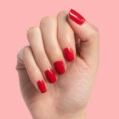Hand with nails painted in vibrant scarlet red Smooch polish against pale pink background for at-home mani