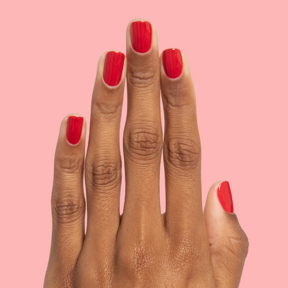 Hand with nails painted in rich scarlet red Smooch polish against a soft pink background for manicure display