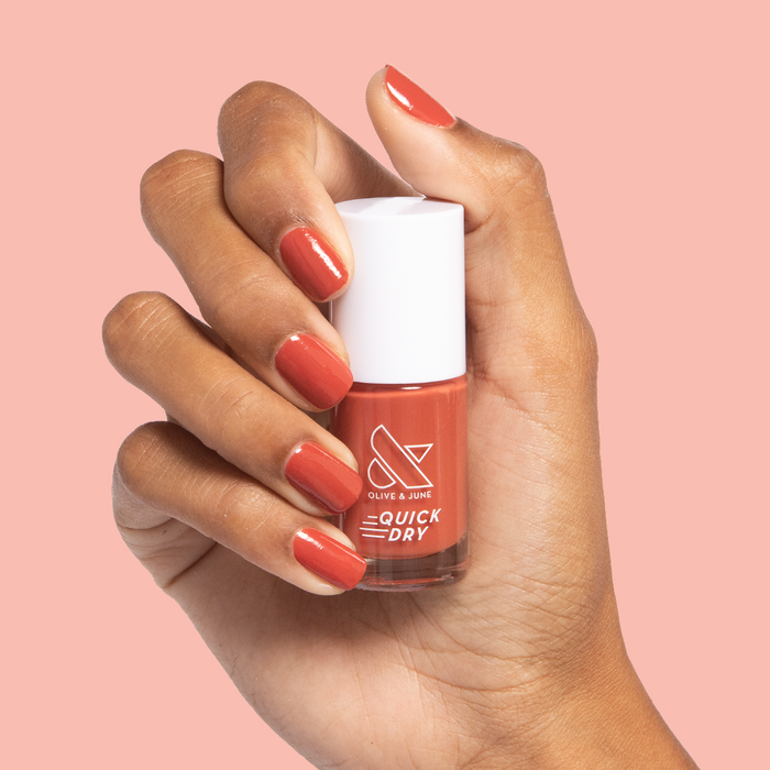 Hand holding Olive and June Southwest quick dry polish bottle with matching warm terracotta manicure on nails