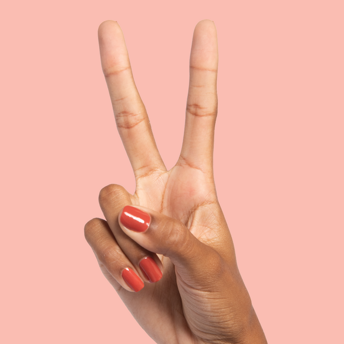 Hand with medium-length nails painted in warm Southwest polish showing a peace sign against a peach background