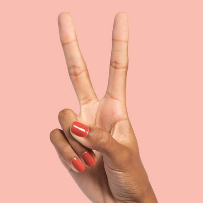 Hand with medium-length nails painted in warm Southwest polish showing a peace sign against a peach background