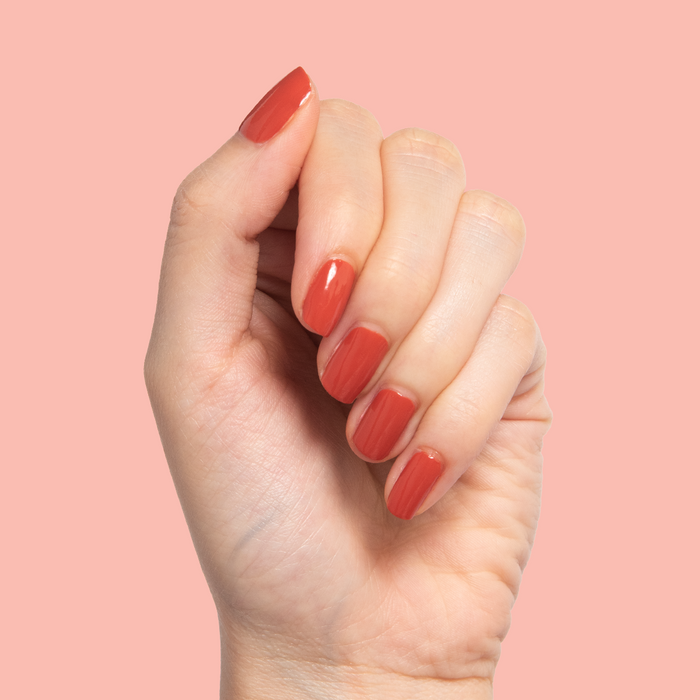 Hand with short nails painted in warm Southwest polish showcasing a smooth at-home mani against a peach background