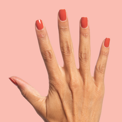 Hand displaying nails painted in warm terracotta Southwest polish for an at-home mani on a peach background