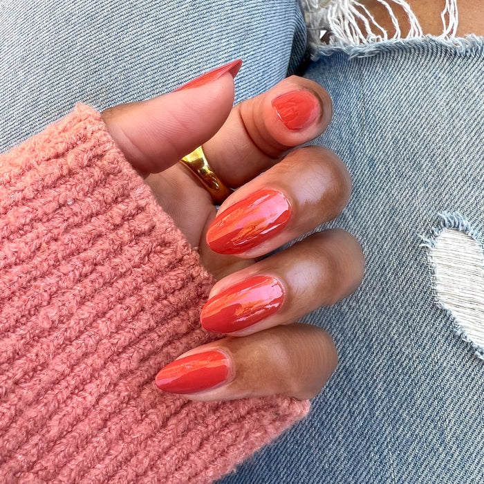 Hand with almond-shaped nails painted in glossy Southwest polish wearing a pink sweater and gold ring over ripped jeans