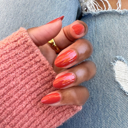 Hand with almond-shaped nails painted in glossy Southwest polish wearing a pink sweater and gold ring over ripped jeans