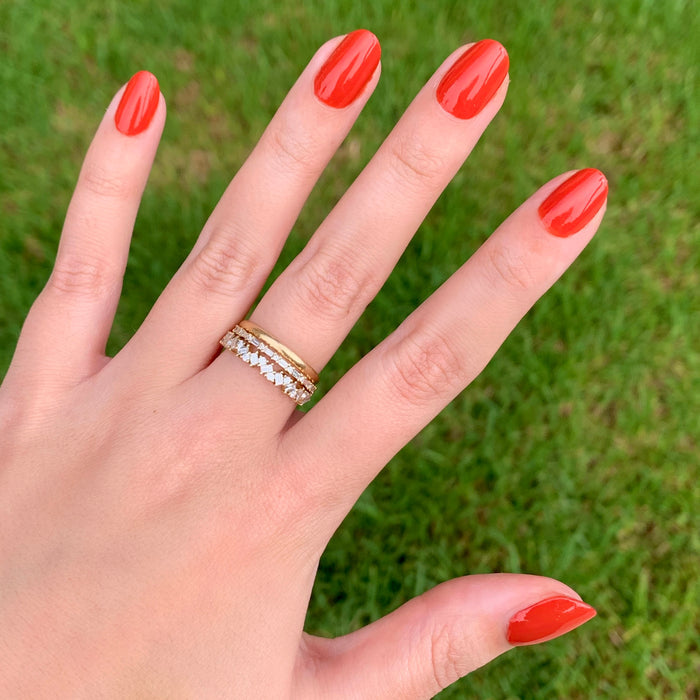 Hand with nails polished in glossy Southwest shade wearing gold and diamond rings outdoors on green grass background
