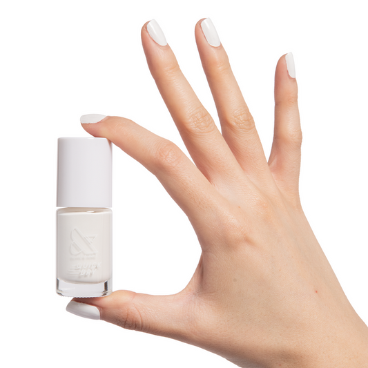 Hand with nails painted in crisp white Swan polish holding a bottle of quick dry nail polish for fresh at-home manis