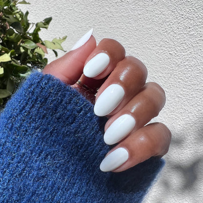 Hand with nails painted in smooth white Swan polish worn with cozy blue sweater for polished at-home manicure