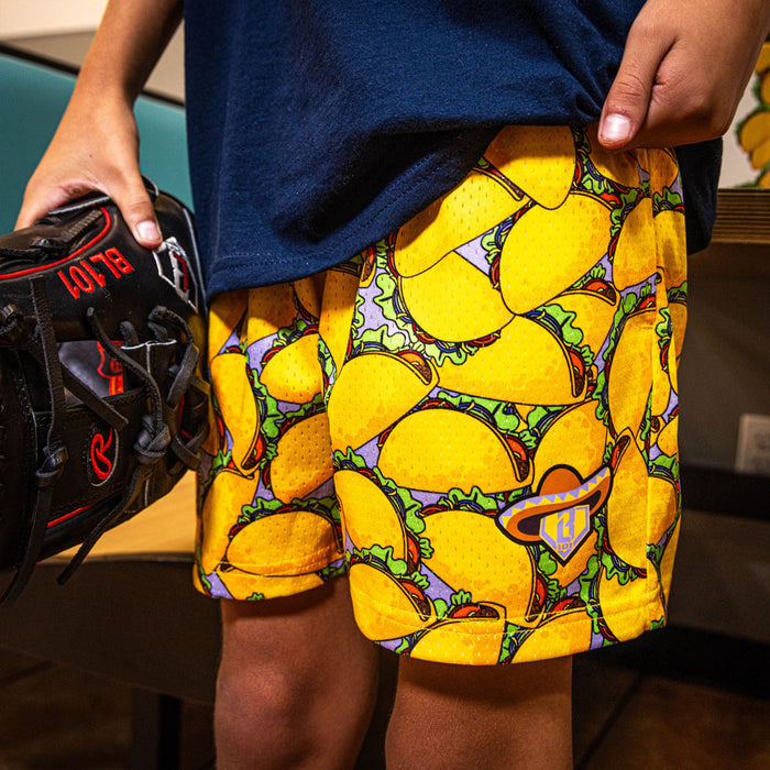 Youth model wearing yellow youth shorts with “Taco” design