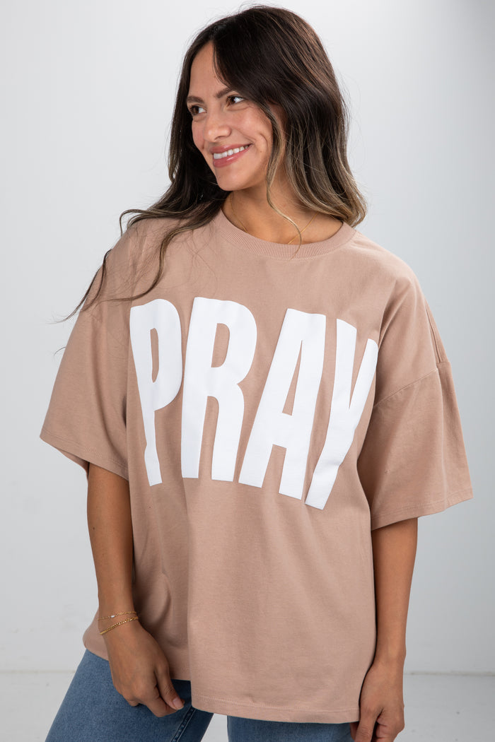 Woman wearing a beige t-shirt with 'PRAY' printed in white on a plain background
