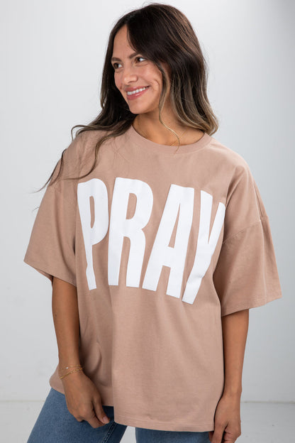 Woman wearing a beige t-shirt with 'PRAY' printed in white on a plain background
