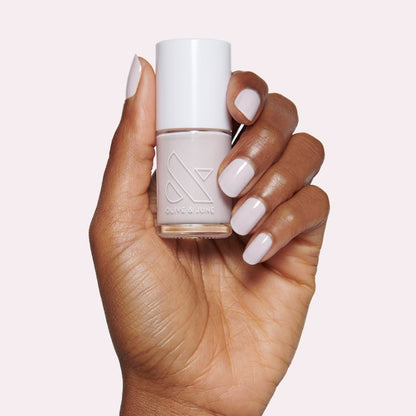 Hand with nails painted in neutral lavender grey The Usual polish holding Olive and June bottle on light background