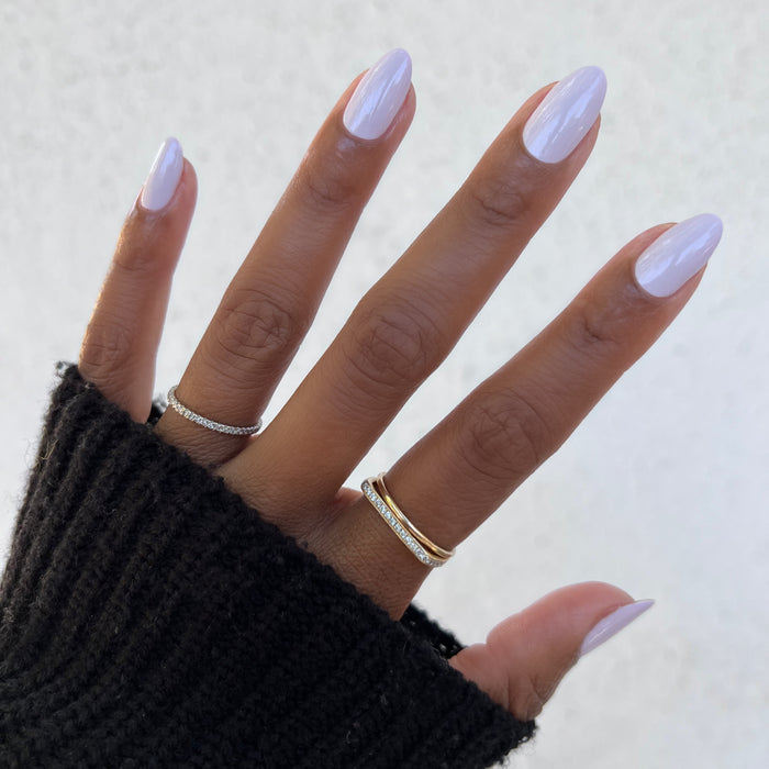 Hand with glossy nails painted in soft neutral lavender grey The Usual polish wearing delicate gold rings and cozy sweater