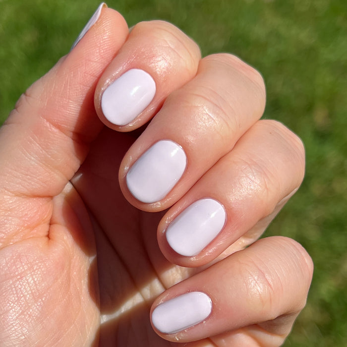 Hand with short nails painted in smooth glossy The Usual neutral lavender grey polish outdoors in natural light